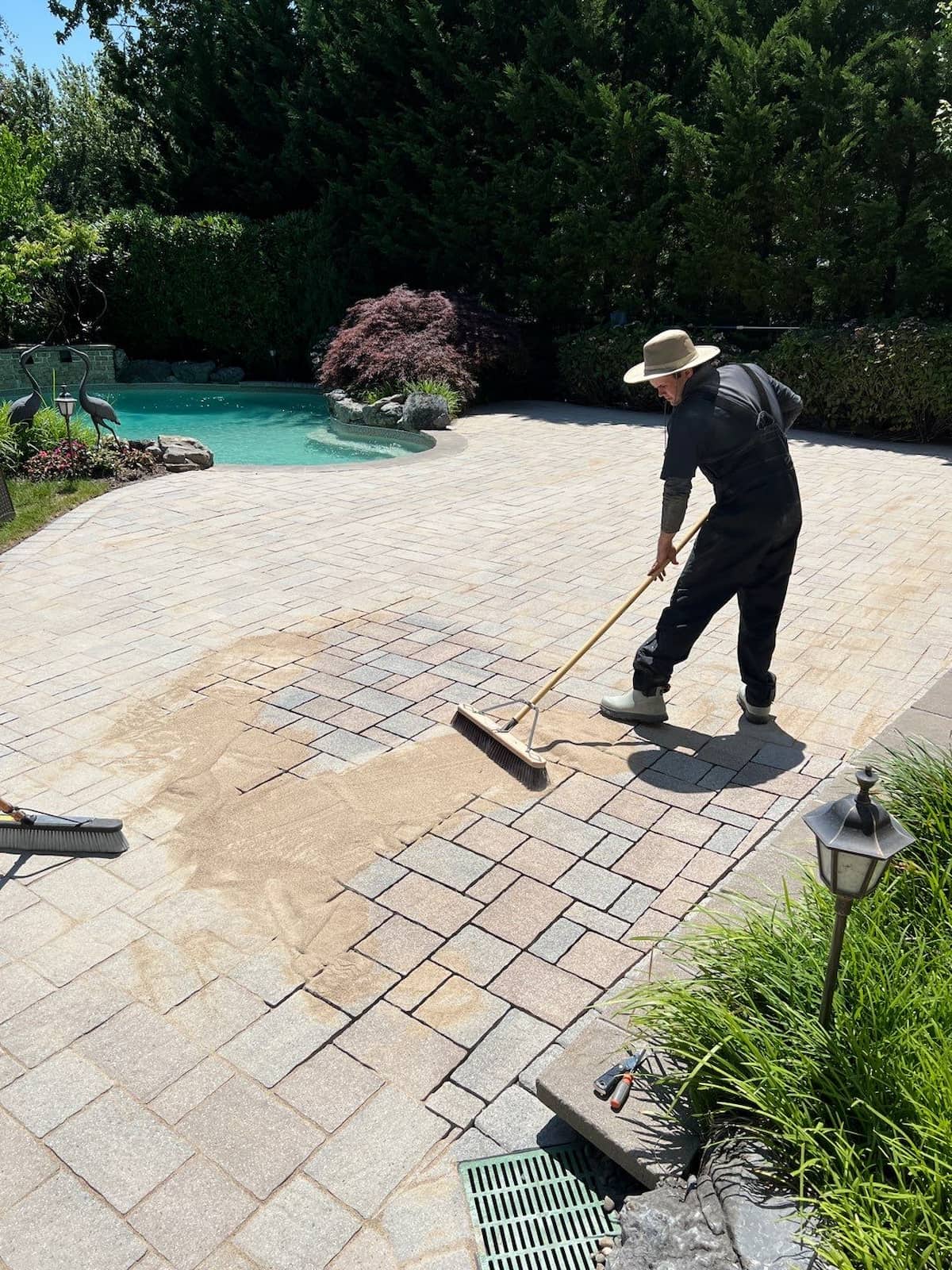 Matthew hand sweeping polymeric sand into paver joints on a residential pool deck — Nassau County Long Island