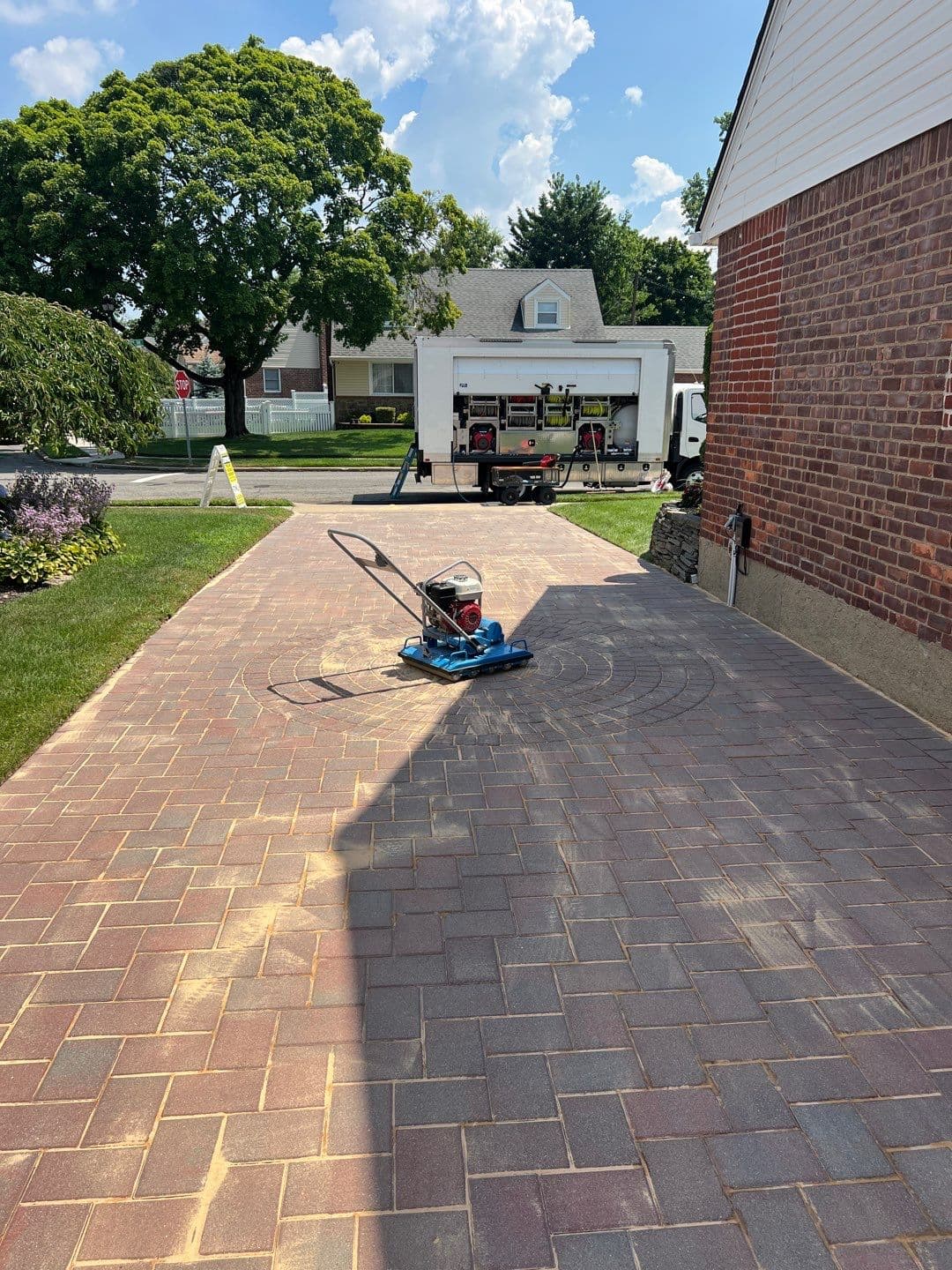 Excess polymeric sand on paver driveway surface before compaction with Bartell vibratory roller — paver restoration by Pressure Wash Long Island, Nassau County