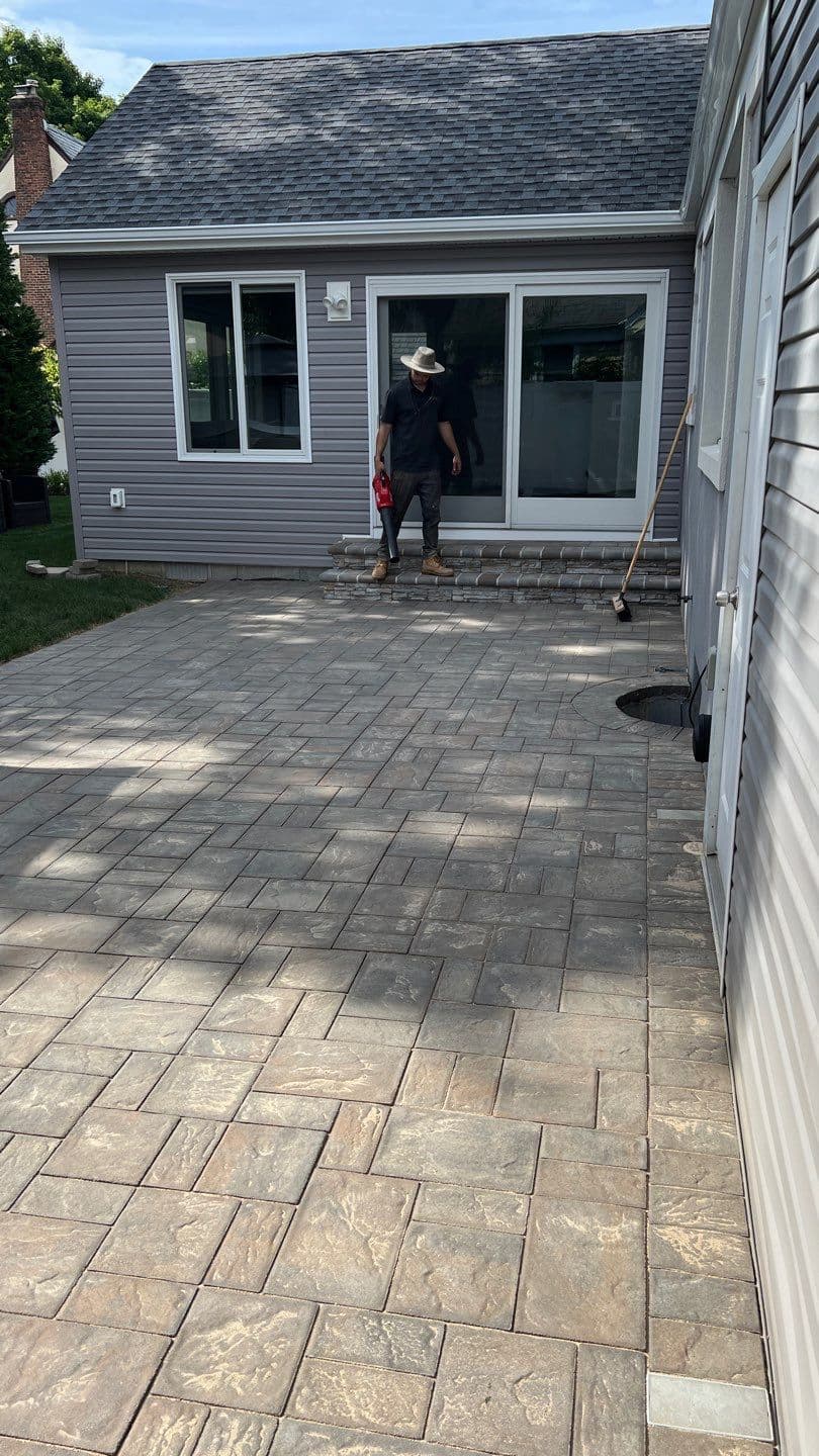 Matthew clearing excess sand from a residential paver patio surface using a blower — paver sanding restoration by Pressure Wash Long Island, Nassau County NY